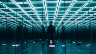 Person stands in a blue neon mirrored room, surrounded by endless reflections representing the multiple complexities of Ai Strategy in Scotland.