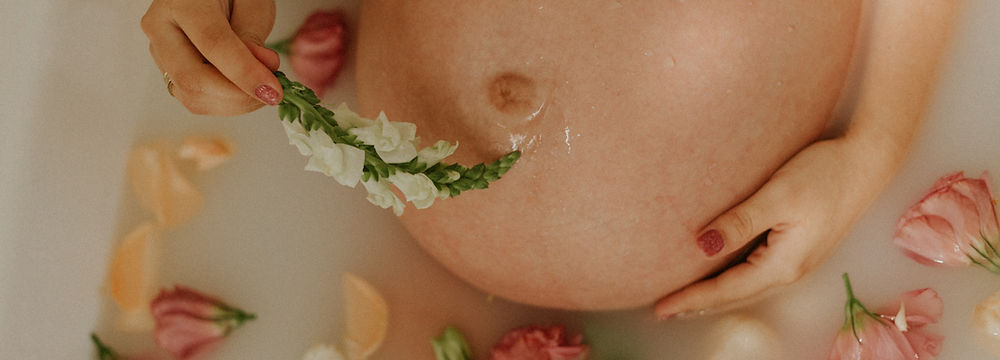 Pregnant woman relaxes in bath surrounded by flowers