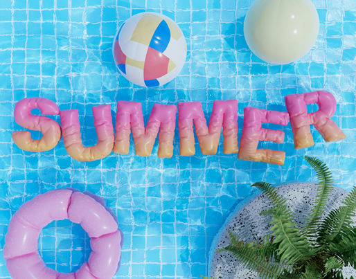 Colorful poolside summer scene featuring the word “SUMMER” spelled out in large inflatable-style letters floating on bright blue pool water, surrounded by pink pool floats and tropical accents.