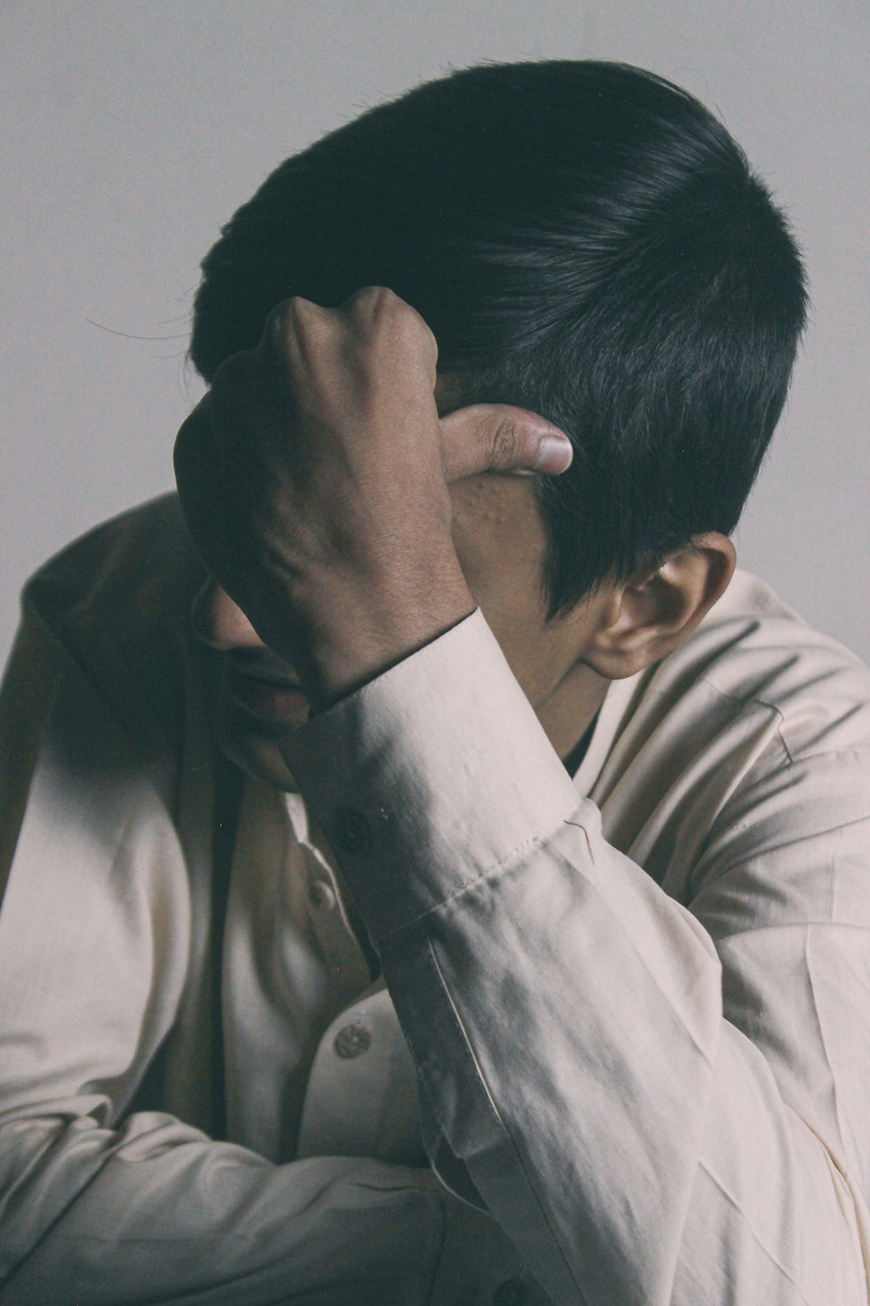 A South Asian male leans on his elbow and anxiously thinks to himself.