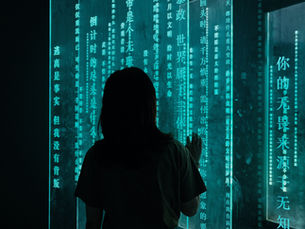 Silhouette of a person facing illuminated vertical screens with glowing teal text in a dark room, creating a mysterious atmosphere.