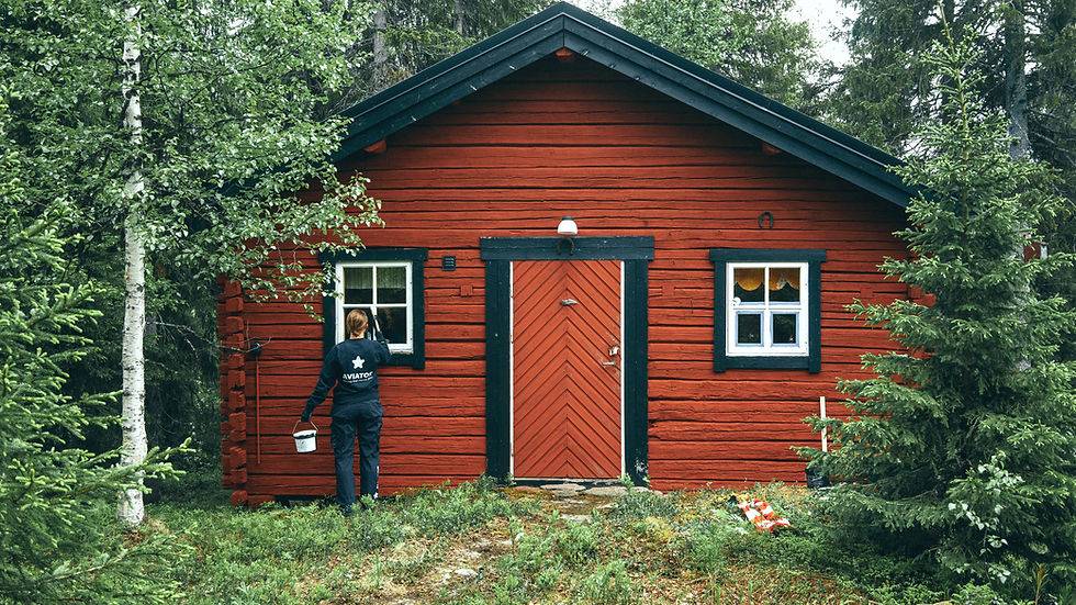 Picture of a traditional Swedish wooden house, in red color, with a person painting the house.