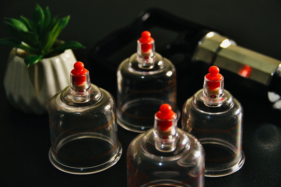 Four transparent cupping therapy cups with red tops on a dark surface, with a small green plant in a white pot nearby.