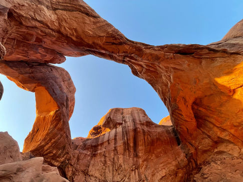 A red rock arch formation against a pale blue sky in the desert of Utah.