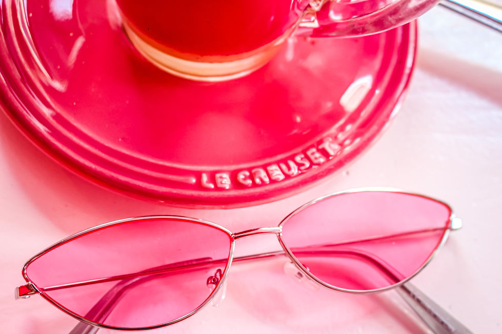 Pink sunglasses and a pink teacup with saucer labeled "Le Creuset" on a pink surface, creating a vibrant, playful mood.