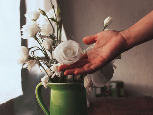 Green vase full of white flowers and a hand touching them appreciatively.
