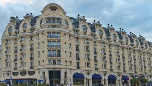 Grand facade of the historic Lutetia Hotel in Paris, showcasing its elegant architecture and curved rooftop windows under a cloudy sky.