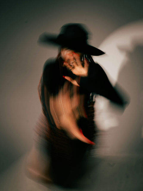 A person in a black hat, red nails, and black attire blurred by motion