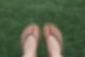 Feet wearing beige flip-flops with pink straps rest on lush green grass