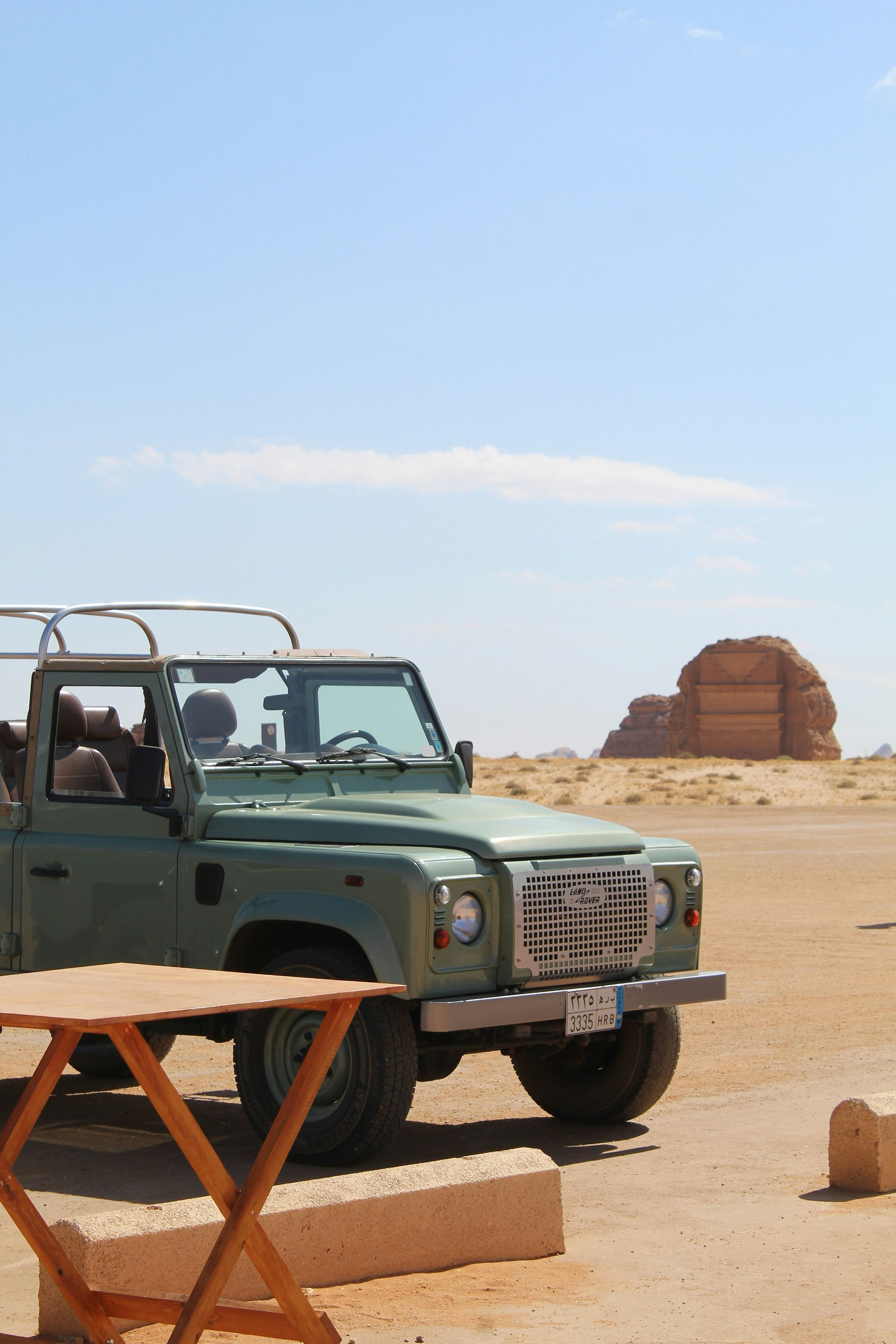 Véhicule tout-terrain vert stationné dans le désert près des formations rocheuses d'Al-Ula, en Arabie saoudite, sous un ciel bleu azur.