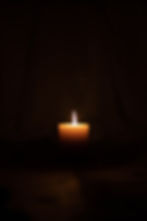 A solitary lit candle in darkness casts a warm glow, creating a tranquil and serene atmosphere. No text or patterns visible.
