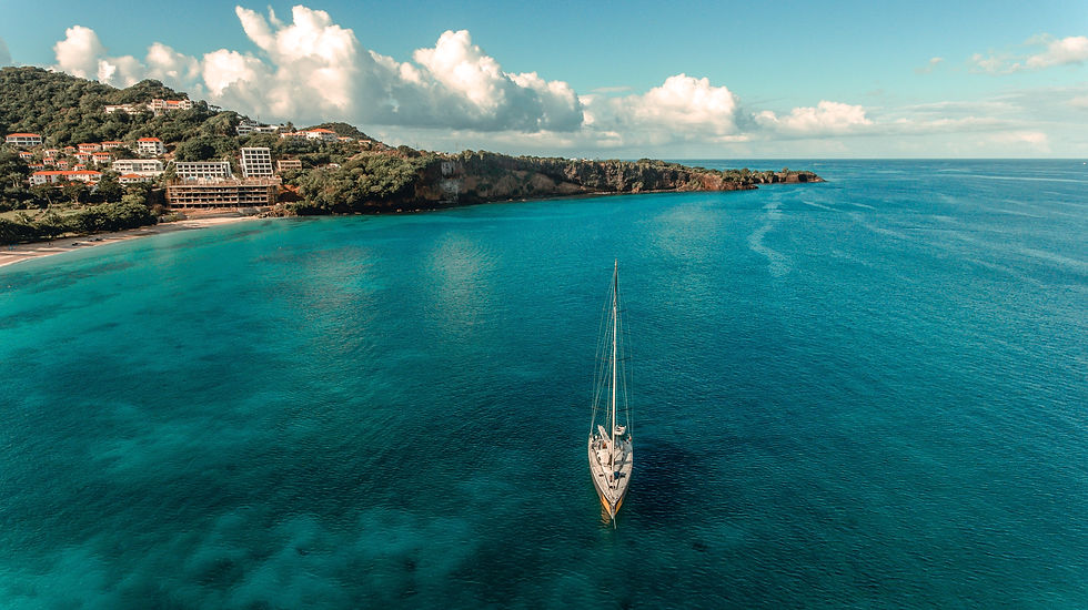 Sailboat on teal sea near lush coastline with colorful houses. Blue sky and puffy clouds create a serene and peaceful mood.