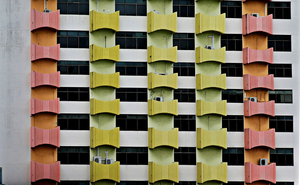 Colorful apartment building facade with pink and yellow balconies and dark windows in a geometric grid.