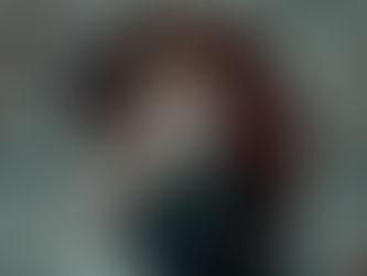 Hand holding ace of diamonds among floating playing cards, person blurred in background, red and black colors prominent.