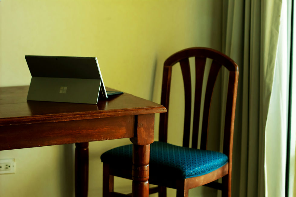 Tablet on a wooden table, with a blue-patterned chair beside it. Neutral walls and curtains create a calm, cozy setting.