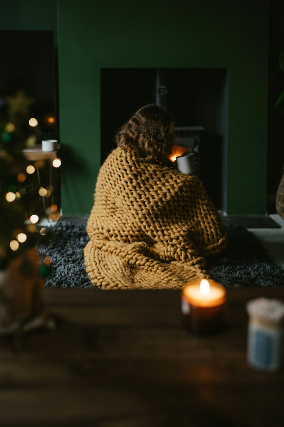 Woman wrapped in a cozy blanket sipping a warm drink in a softly lit room at night during a calming wind-down routine before bed