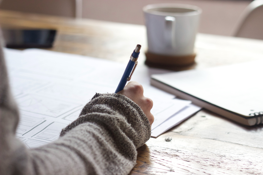 Photo of a woman's hand writing on a piece of paper on the table