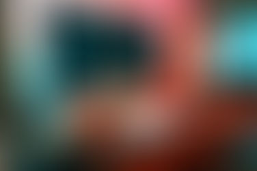 Hand holds bitcoin coin in front of a computer screen displaying a rising stock chart. Red and teal lighting creates a dynamic mood.