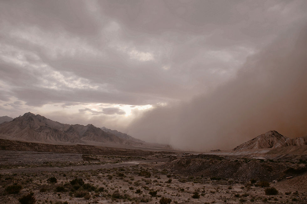 Desert mountains under dark storm clouds, with sunlight breaking through and a dust wall rolling across the valley.