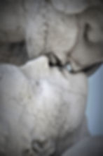 A close-up captures the intimate moment of two marble statues embodying a timeless and tender embrace, their lips nearly touching.