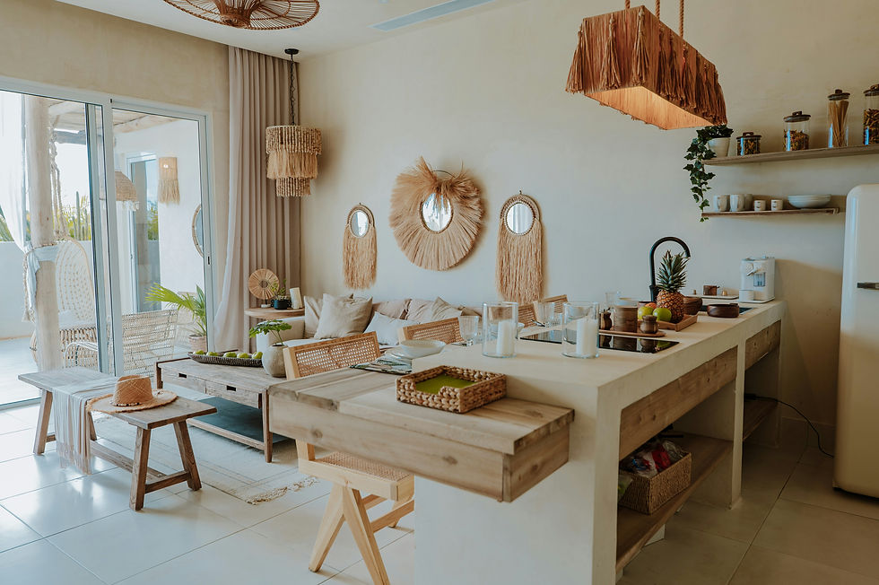Cozy living room and kitchen with rattan decor, wicker lights, fruit bowl, and plants. Bright, airy feel with earthy tones.