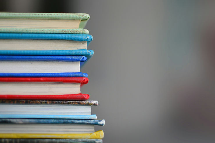 Stack of colorful books with red, blue, and green spines. Neutral gray background, conveying a calm and organized atmosphere.