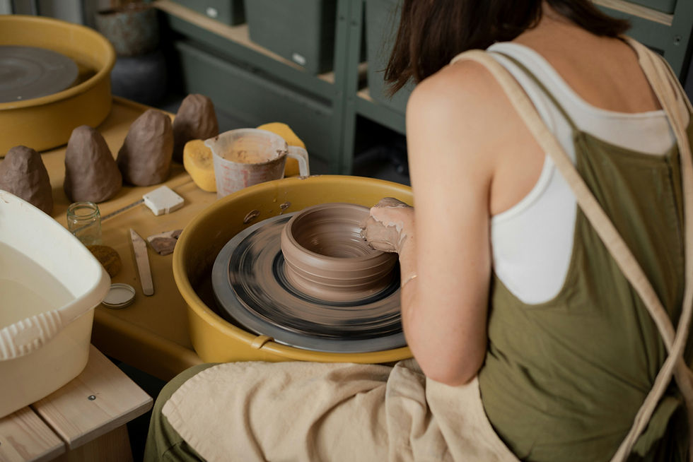 Woman in green apron shapes a clay pot on a spinning pottery wheel in a studio with mustard tubs and tools.