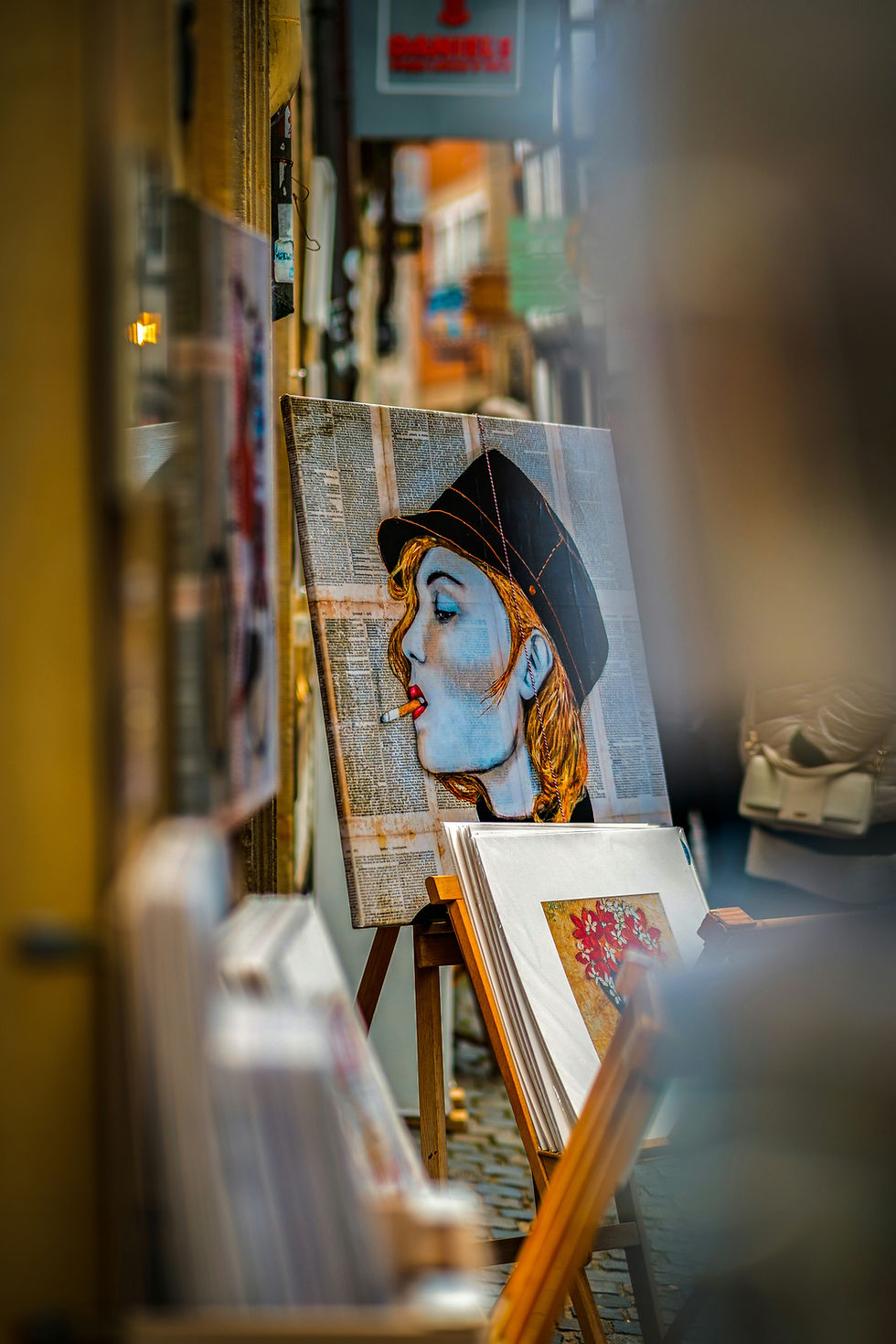 A vibrant mixed media artwork depicting a stylish figure with a cigarette, set against a background of newspaper clippings, displayed on an easel amidst a bustling street scene.