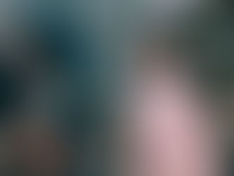 A young girl poses happily in front of a decorated Christmas tree while someone takes her photo.