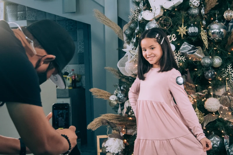Father taking Picture of daughter in front of christmas tree