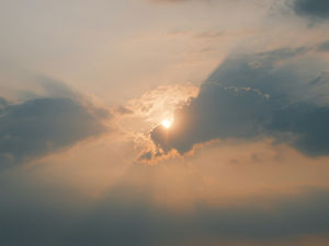 Sun sets behind dark clouds, casting beams of warm orange and yellow light in the sky, creating a serene, dramatic atmosphere.