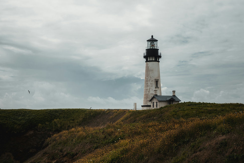 Yaquina Head Lighthouse on a grassy cliff under a cloudy sky