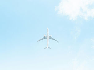 Underside view of a white commercial airplane flying directly overhead against a bright, pale blue sky with faint, soft white clouds.