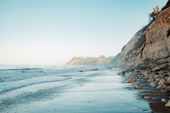 Santa Barbara beach with gentle waves, sandy shore, and towering cliffs under a clear blue sky. Peaceful and serene coastal scene.