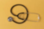 A black stethoscope lies coiled on a mustard yellow background, creating a simple and professional medical-themed image.