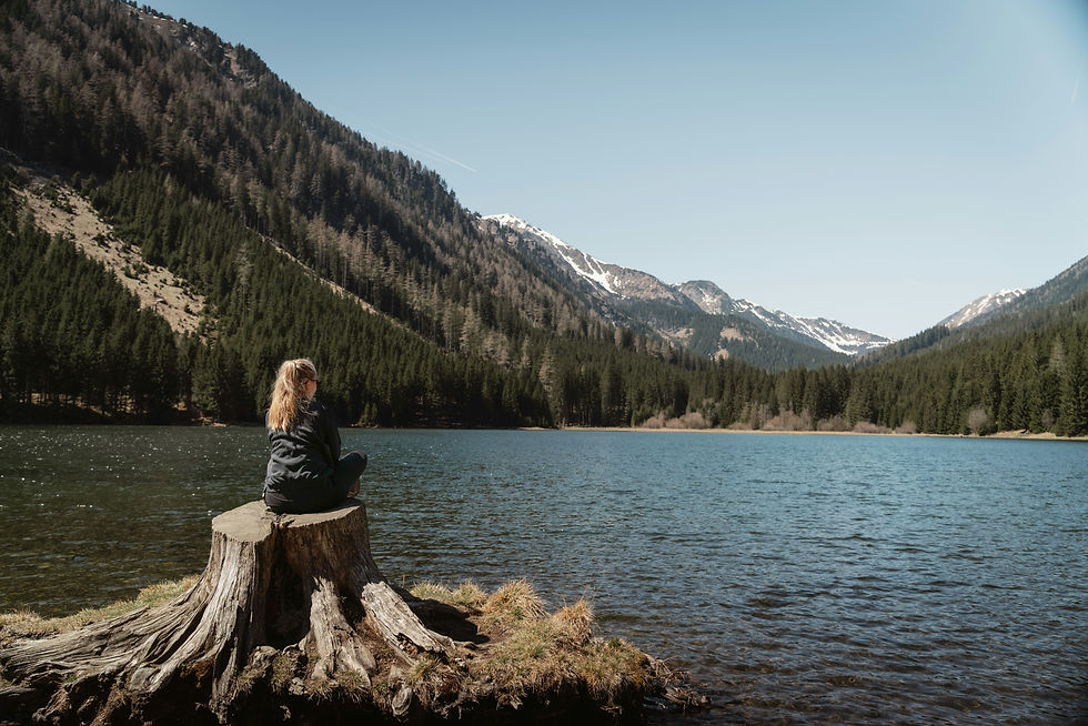 woman sitting on log by lake surrounded by mountains