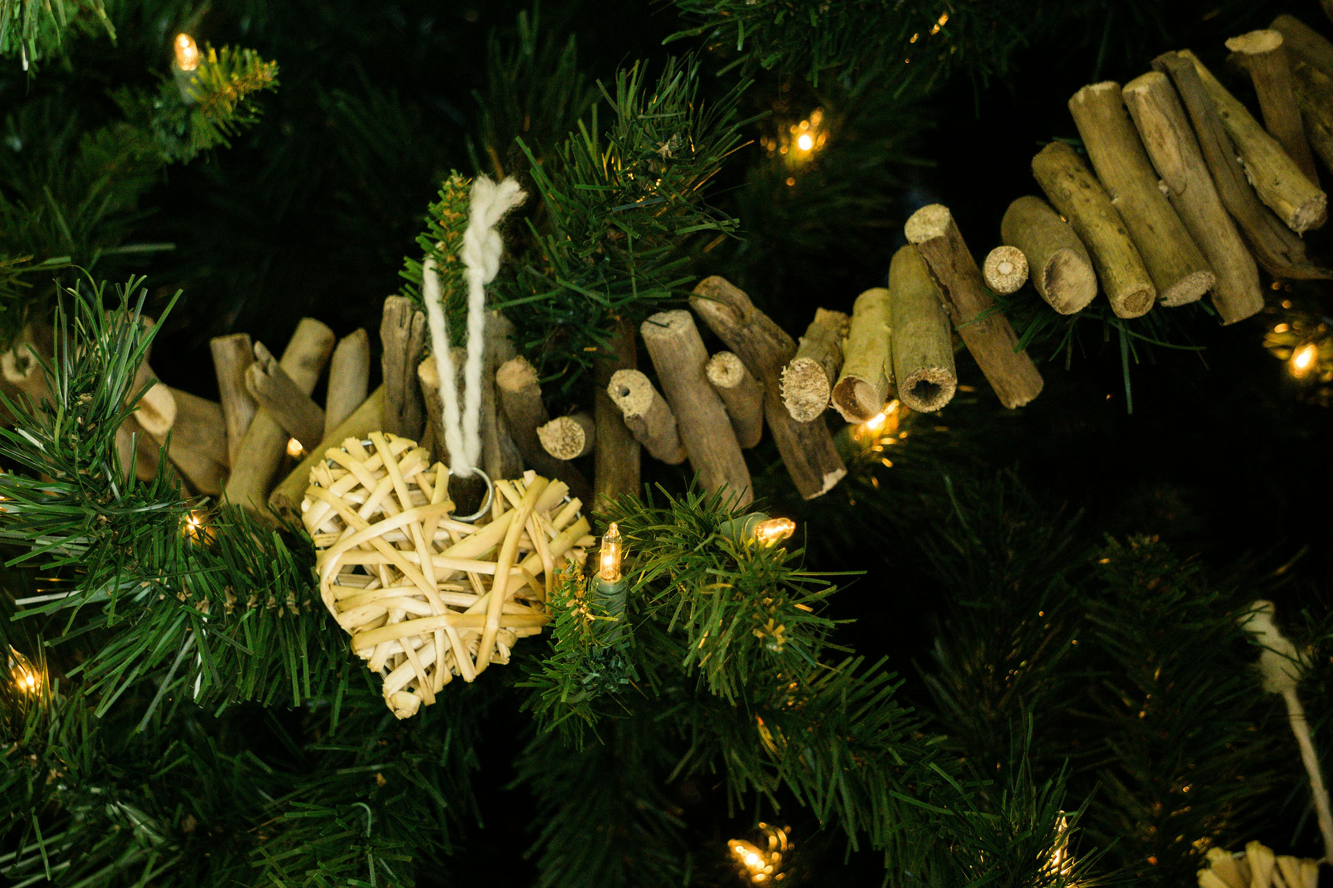 Wooden Christmas tree garland made from short sticks and a woven raffia heart ornament hang on a tree