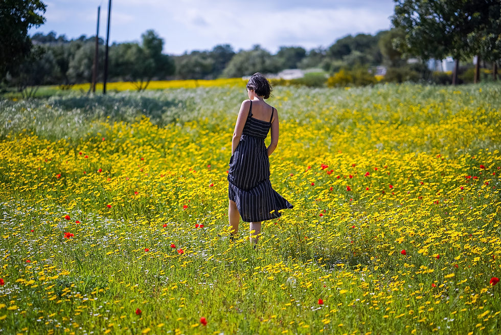 Woman walking through field of wildflowers with hands in pockets of her summer dress.
