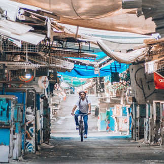 A local cyclist riding through the narrow stone alleys of the Carmel Market in Tel Aviv, showing the urban life of the city.