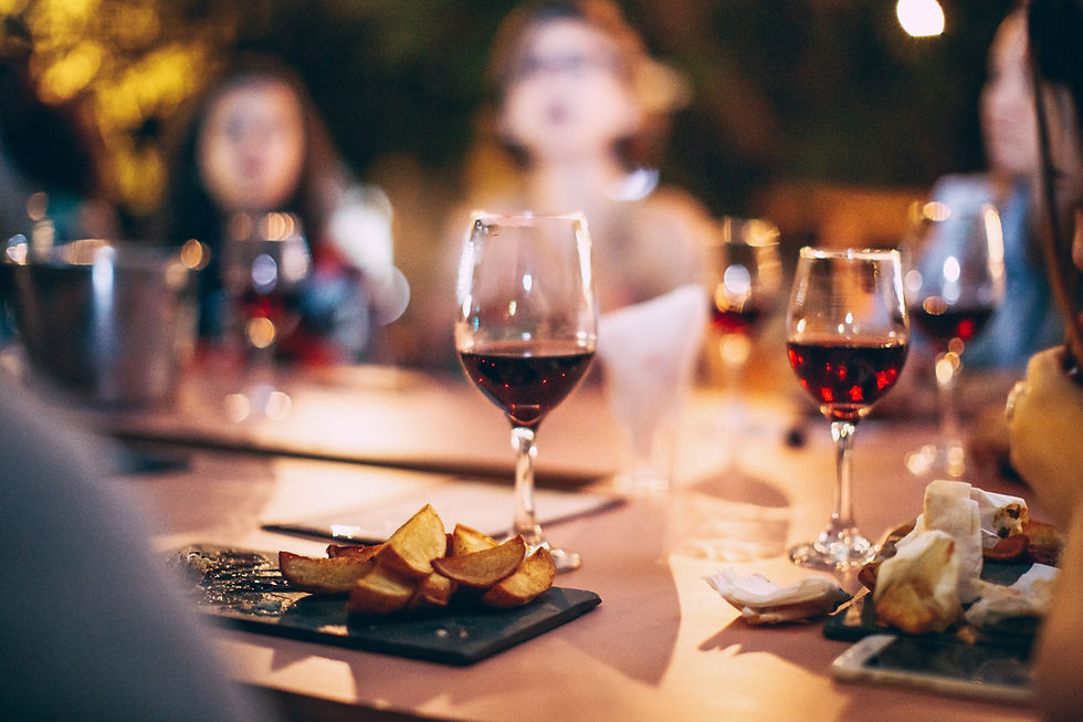 Blurred diners at a warmly lit restaurant table with red wine glasses and appetizers, creating a cozy evening mood.