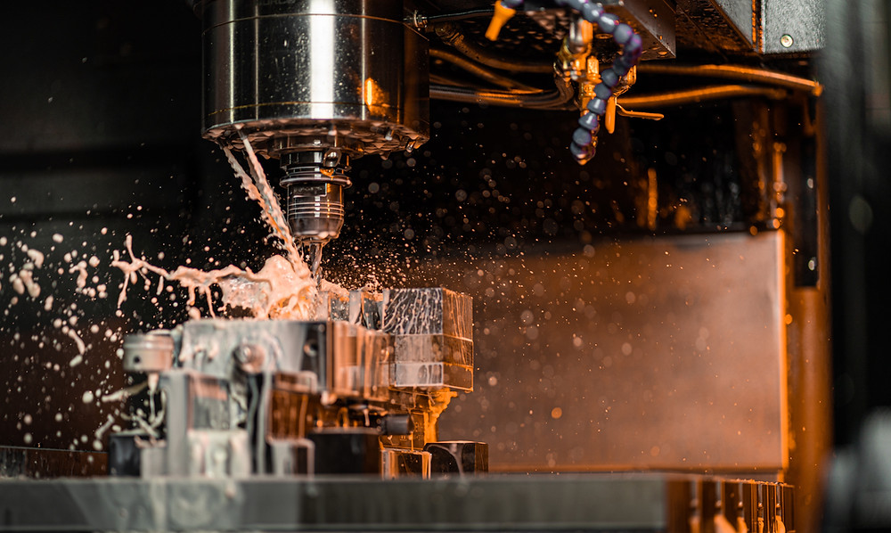 This is a picture of a CNC router, milling on a piece of metal, with coolant splattering away from the work.