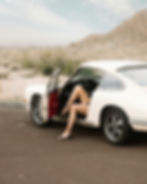 Image by Spencer Davis. Vint white car parked on the size of a ert looking road/ Womans legs stick out of an open car door.