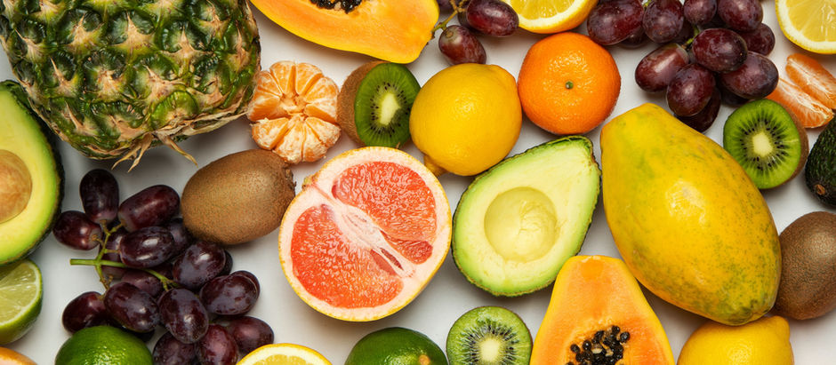Assorted fruits on a white background, including pineapple, papaya, grapes, avocado, citrus, and kiwi, creating a vibrant, fresh display.