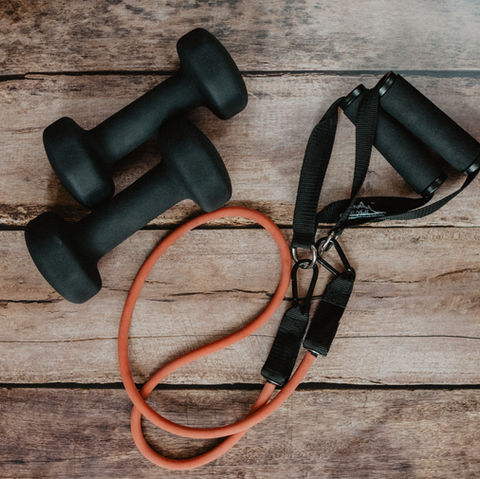 Overhead shot of a small dumbbell and workout bungee cables laid out on a wooden floor.