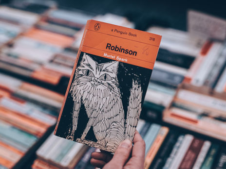 Robinson by Muriel Spark paperback edition held up with a background made out of spine up books