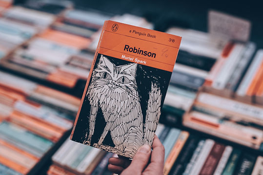 Mass-market paperback with cat illustration to up with background of books with spines up.