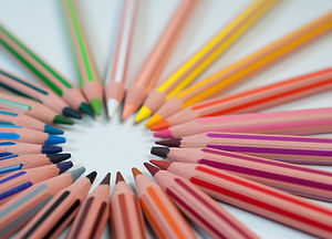 Two dozen colored pencils on a white surface arranged in a circle with the multi-colored points facing to the center. Image by Agence Olloweb