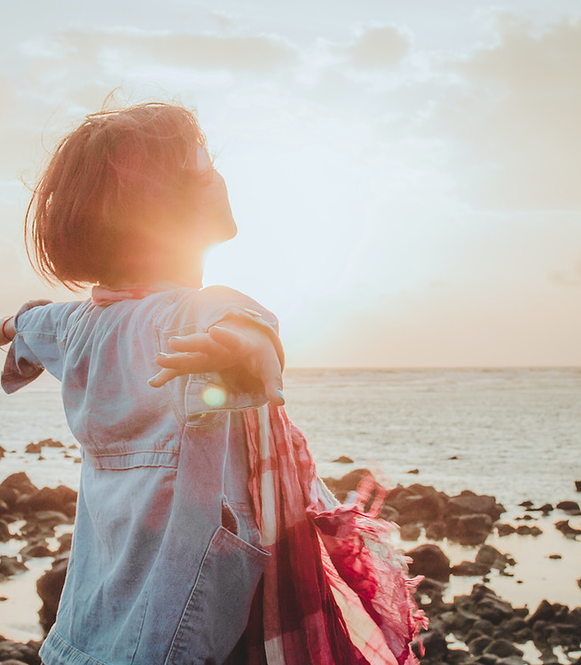 Woman with arms open wide on beach at sunset