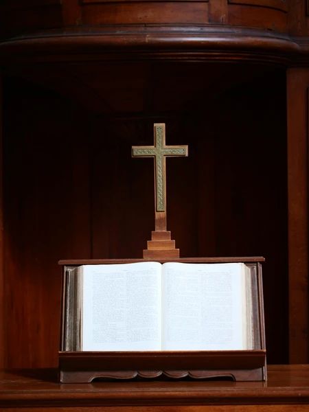 An open Bible on a table beneath a wooden cross in a church sanctuary