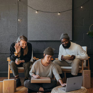 Trois personnes assises dans un salon chaleureux, échangeant par visioconférence sur un ordinateur portable, entourées de cadeaux emballés et d’une ambiance conviviale.